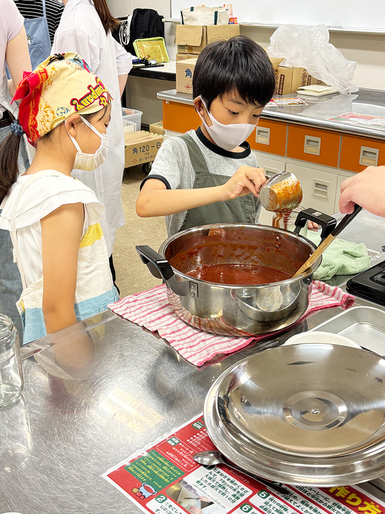 完成したトマトケチャップを瓶詰めする子供