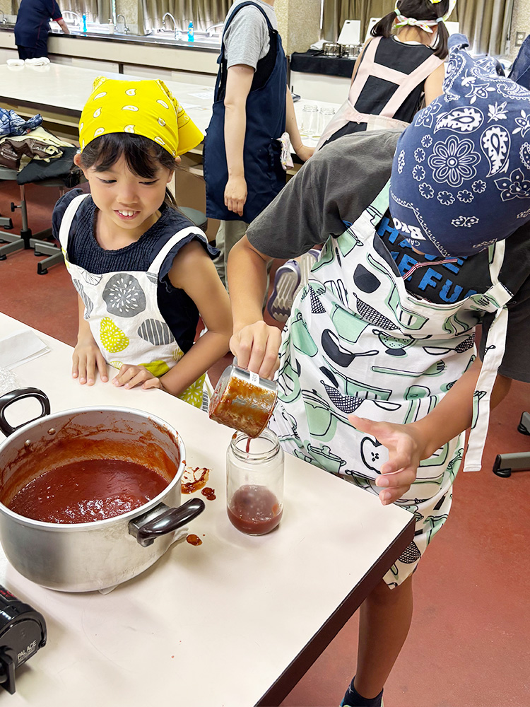 完成したトマトケチャップを瓶詰めする子供