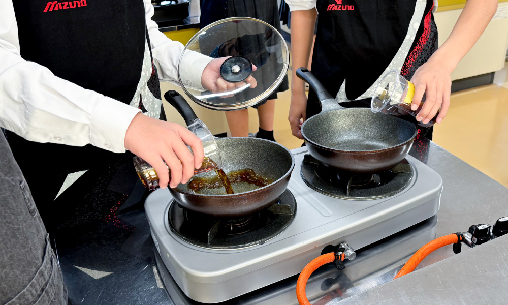 古知野中学校の出前講座 2025年 フライパンに調味料を入れる様子
